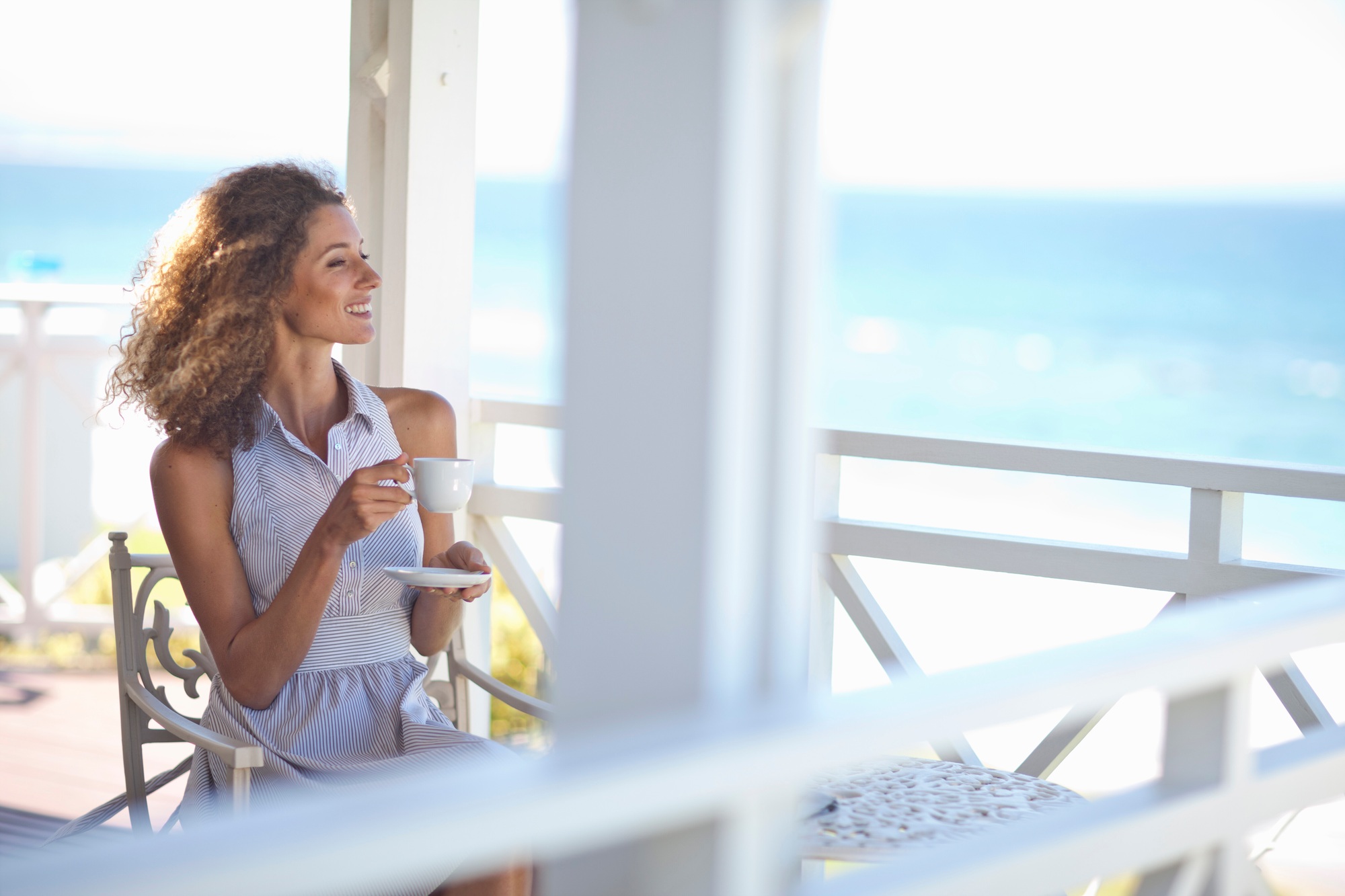 Young woman with coffee gazing out to sea from beach house balcony